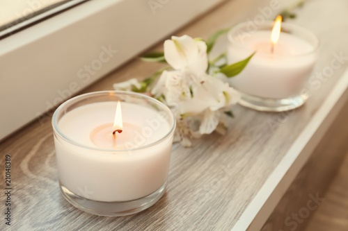 Burning wax candles with flowers on windowsill
