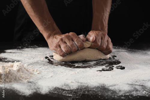Fototapeta Naklejka Na Ścianę i Meble -  Man kneading dough on black background