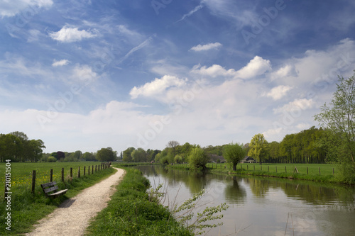Authentic Dutch landscape with river Kromme Rijn, walkway, wooden bench, clouds and trees