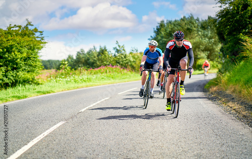 Cyclists racing on country roads on a sunny day in the UK.