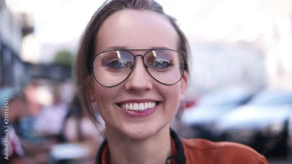 Gorgeous close up view of a young, blonde girl looking at the camera and smiling, Wearing a stylish, modern glasses. Happy, carefree. Outdoors Gorgeous close up view of a young, blonde girl looking at the camera and smiling, Wearing a stylish, modern glasses. Happy, carefree. Outdoors