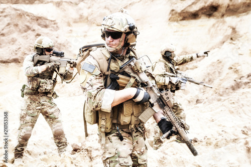 Tableau sur toile Group of well equipped US army commandos armed with assault rifles, moving through sandy terrain or desert
