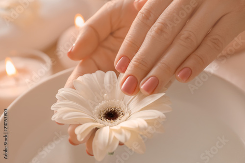 Young woman with fresh manicure and beautiful flower after treatment in spa salon, closeup