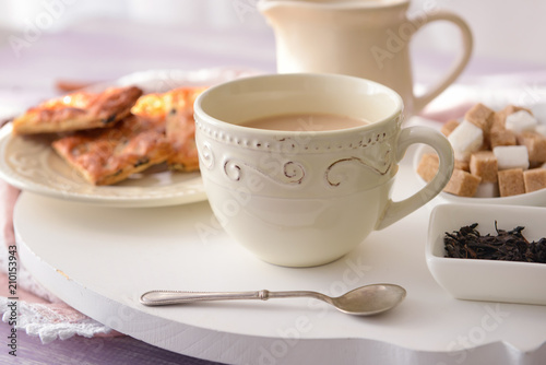 Cup of aromatic tea with milk and sweets on table