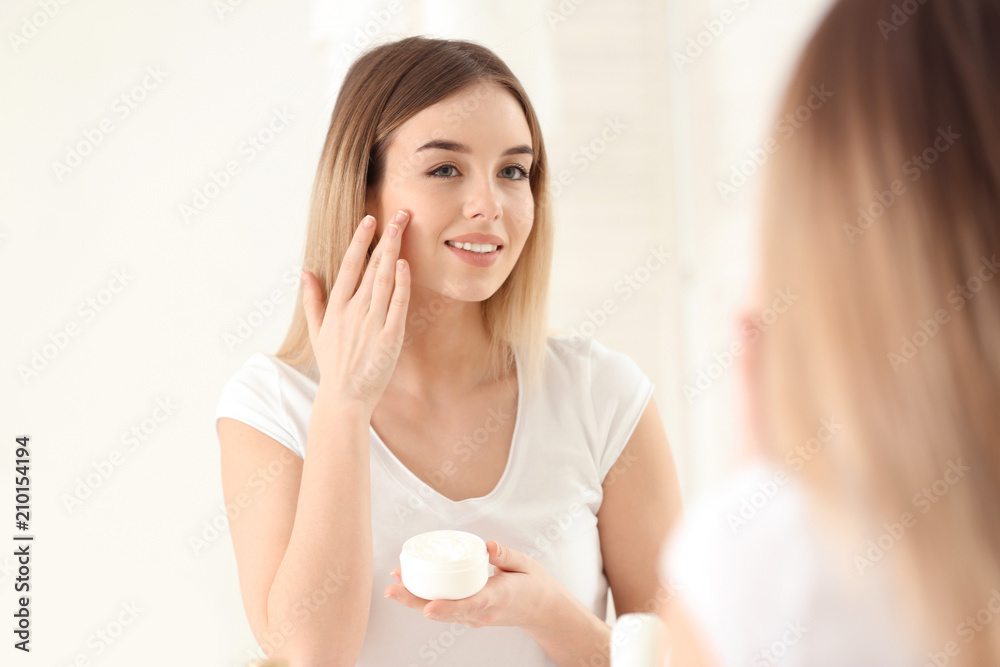 Beautiful young woman applying cream in morning