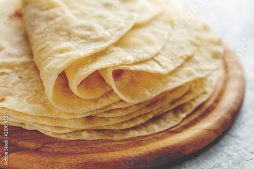 Stack of homemade wheat flour tortilla wraps on wooden cutting board. photo