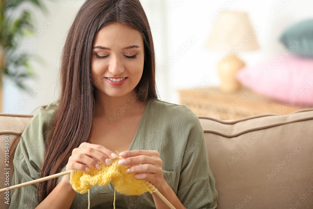 Young woman sitting on sofa and knitting warm sweater indoors Young woman sitting on sofa and knitting warm sweater indoors