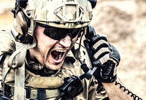 Foto Special forces soldier, military communications operator or maintainer in helmet and glasses, screaming in radio during battle in desert