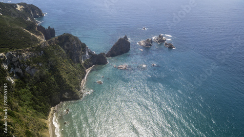 Aerial view of a rocky coastline overlooking the Mediterranean Sea. On the mountain grows a forest with many trees and there is some big rock in the blue and azure sea.