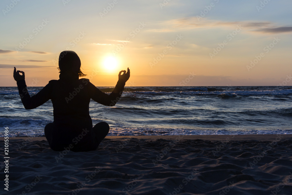 silhouette of Young woman sitting back, meditate in lotus yoga pose outdoor, on the beach.