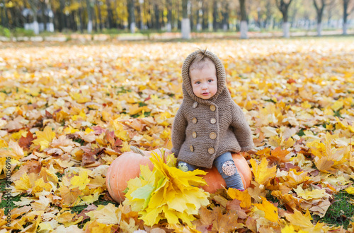 Little girl sits with pumpkin in the autumn city park.