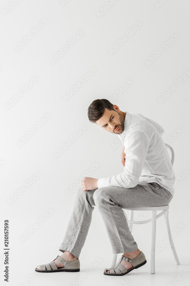 man in linen clothes sitting on chair looking away isolated on grey background man in linen clothes sitting on chair looking away isolated on grey background