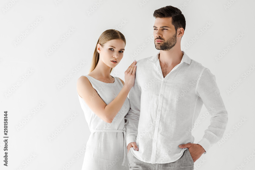 attractive woman in linen white dress embracing boyfriend with hands in pockets isolated on grey background