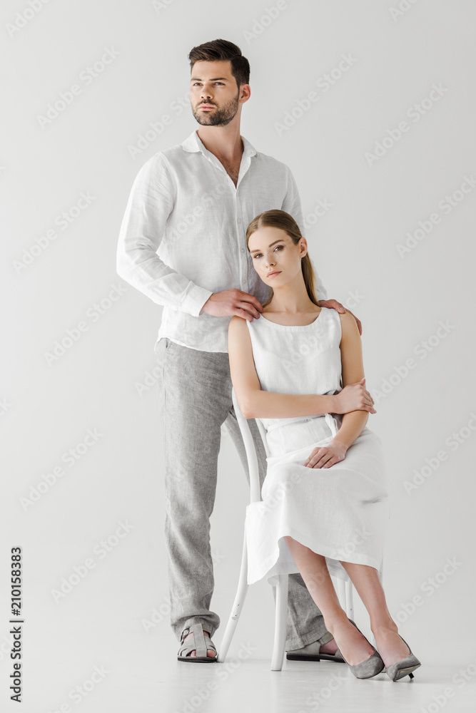 handsome man embracing girlfriend in linen white dress sitting on chair isolated on grey background handsome man embracing girlfriend in linen white dress sitting on chair isolated on grey background