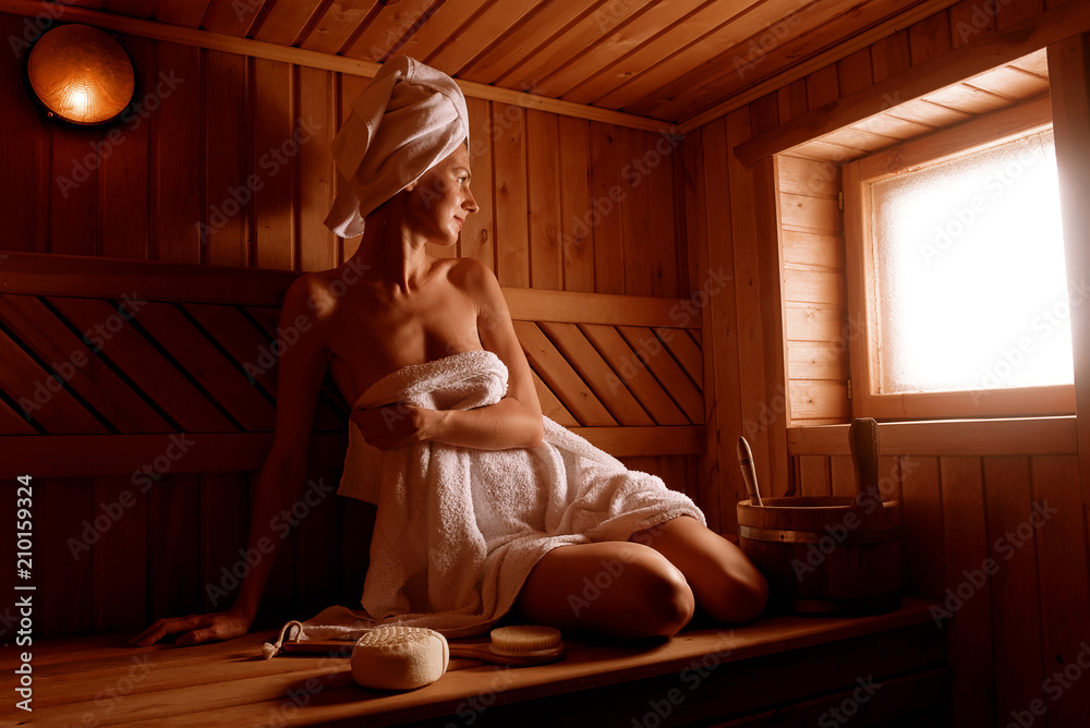 Obraz premium girl in a spa treatment in a traditional sauna with a brush for skin and a washcloth. relaxes wrapped in a white towel