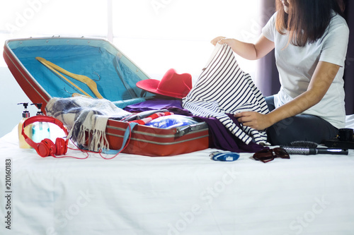 Travel and vacation concept, happiness young woman packing a lot of her clothes and stuff into suitcase on bed prepare for travel and journey trip in holiday