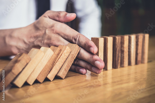 Strategy and successful intervention concept for business, businessman hand Stopping Falling wooden Dominoes effect from continuous toppled or risk photo