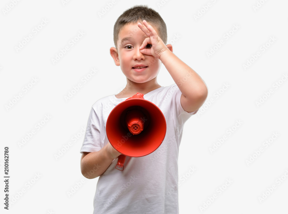 Dark haired little child holding megaphone with happy face smiling doing ok sign with hand on eye looking through fingers Dark haired little child holding megaphone with happy face smiling doing ok sign with hand on eye looking through fingers