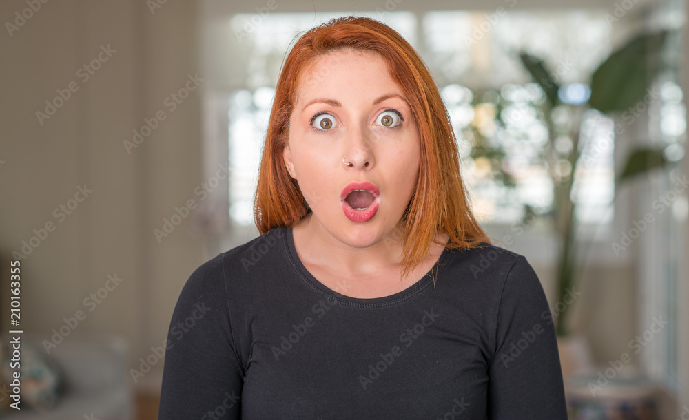 Redhead woman at home scared in shock with a surprise face, afraid and excited with fear expression Redhead woman at home scared in shock with a surprise face, afraid and excited with fear expression