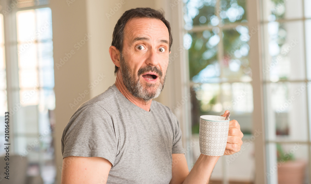 Middle age man drinking coffee in a cup scared in shock with a surprise face, afraid and excited with fear expression