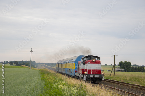 Stara lokomotywa z wagonami piętrowymi pędzi przez pole