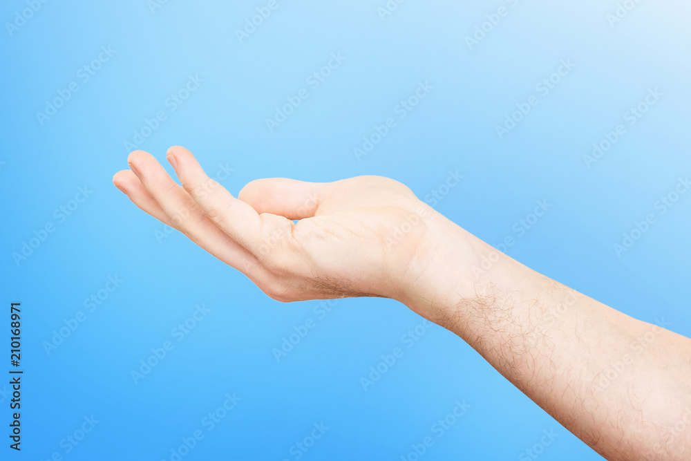 Closeup empty male hand making holding gesture with opened palm isolated at blue background.