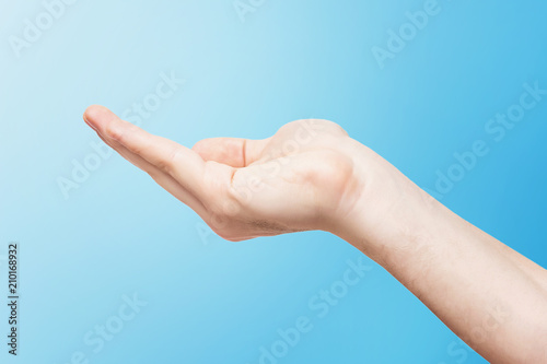 Closeup empty male hand making holding gesture isolated at blue background.