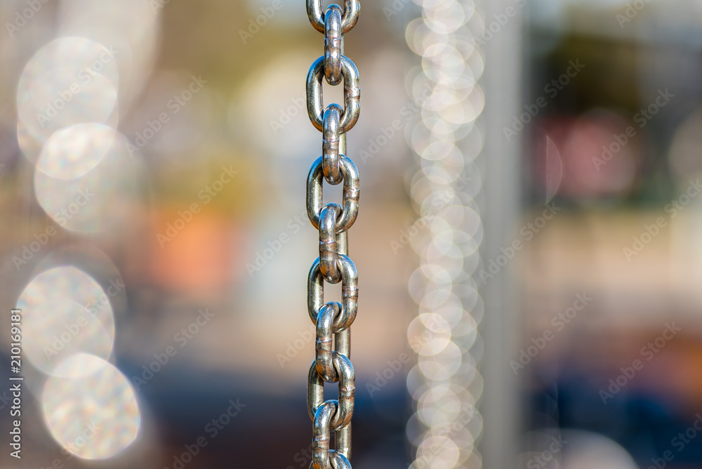 Many vertical hanging stainless steel chains in varying depth of field and focus