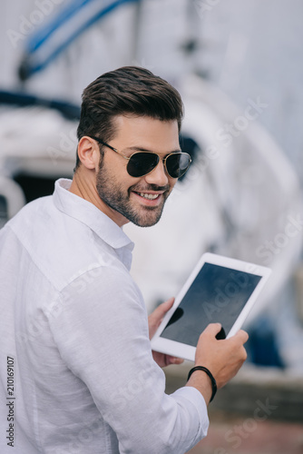 handsome young man in sunglasses smiling at camera while using digital tablet with blank screen © LIGHTFIELD STUDIOS