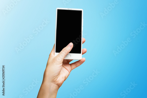 Mockup of female hand holding frameless cell phone with black screen isolated at blue background.