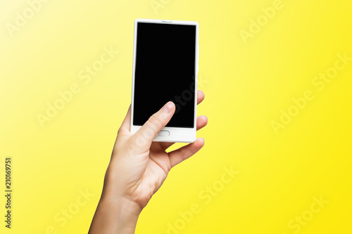 Mockup of female hand holding frameless cell phone with black screen isolated at yellow background.