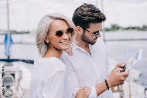 beautiful smiling young couple in sunglasses using digital tablet on yacht © LIGHTFIELD STUDIOS
