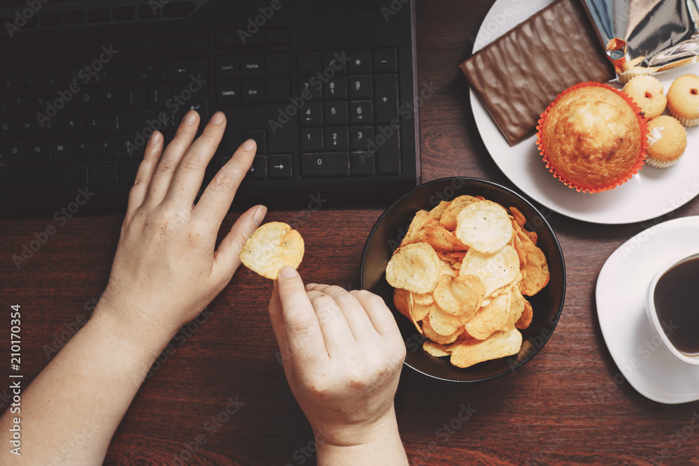 Unhealthy snack at workplace. Hands of woman working at computer and ...
