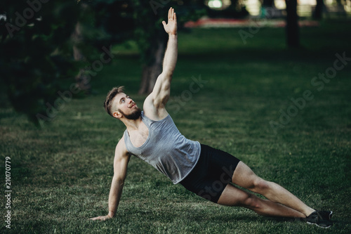 Yoga  endurance training  street workout  fitness  sport  outdoor activity  healthy lifestyle concept. Young fit muscular sportsman doing side plank in morning park