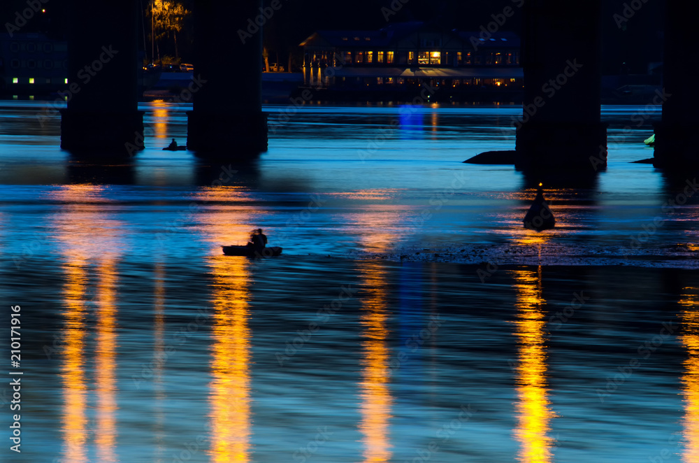 Long exposure shot of fisherman floating in boat on river with lantern lights reflections on twilight
