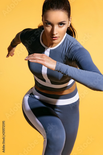 Attractive woman runner in fashionable sportswear on yellow background. Dynamic movement. Close up. Sport and healthy lifestyle