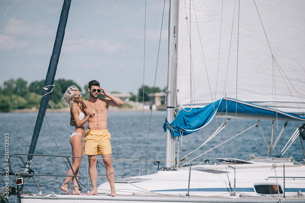 beautiful young couple in swimwear and sunglasses standing together on yacht beautiful young couple in swimwear and sunglasses standing together on yacht