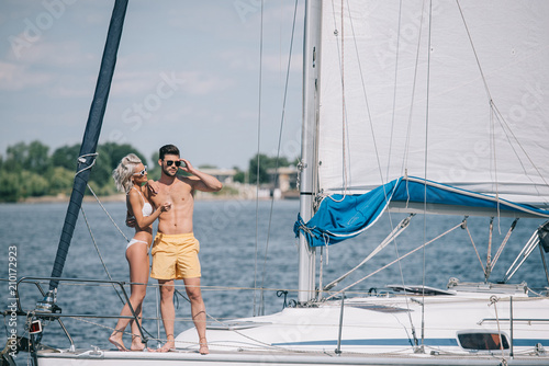 beautiful young couple in swimwear and sunglasses standing together on yacht © LIGHTFIELD STUDIOS