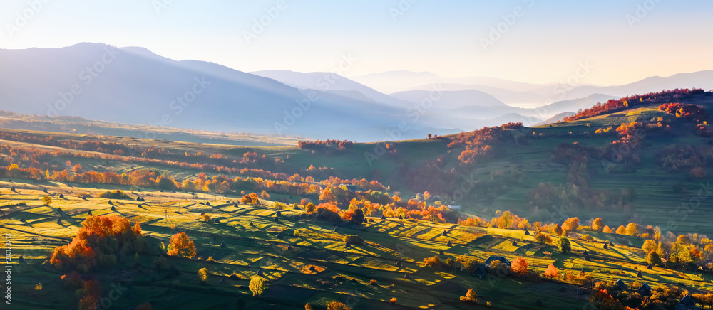 Extraordinary autumn scenery. Green fields with haystacks. Trees covered with orange and crimson leaves. Mountain landscapes. Nice rays of the sun. Location place  Ukrain, Europe.