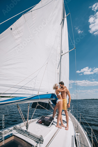 smiling young couple in swimwear embracing on yacht