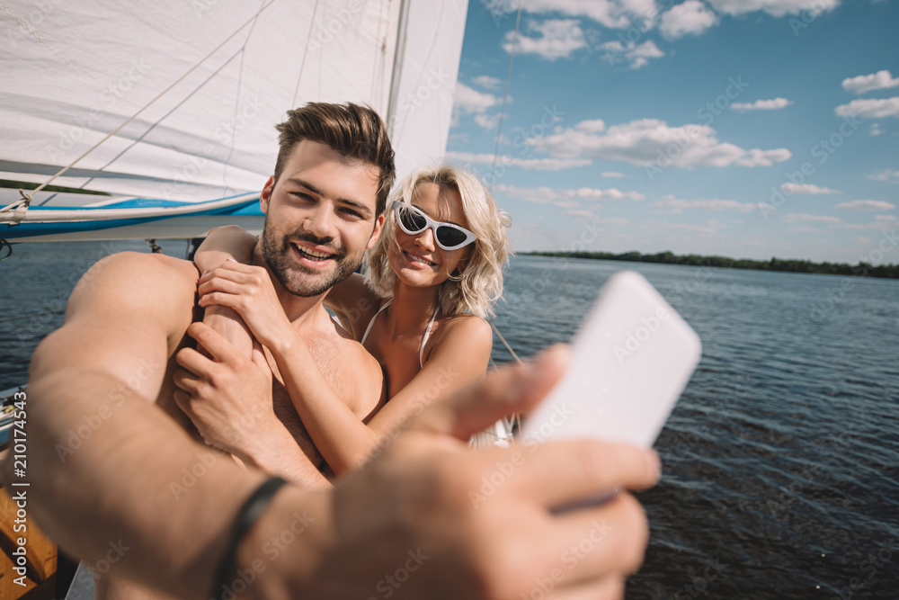 smiling young couple taking selfie on smartphone on yacht