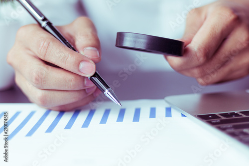 Businessmen use a magnifying glass to analyze the company's data and statistics from the chart.