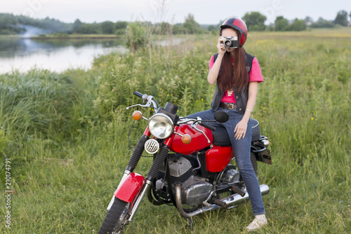 Girl in a retro helmet sitting on a vintage motorcycle with a camera