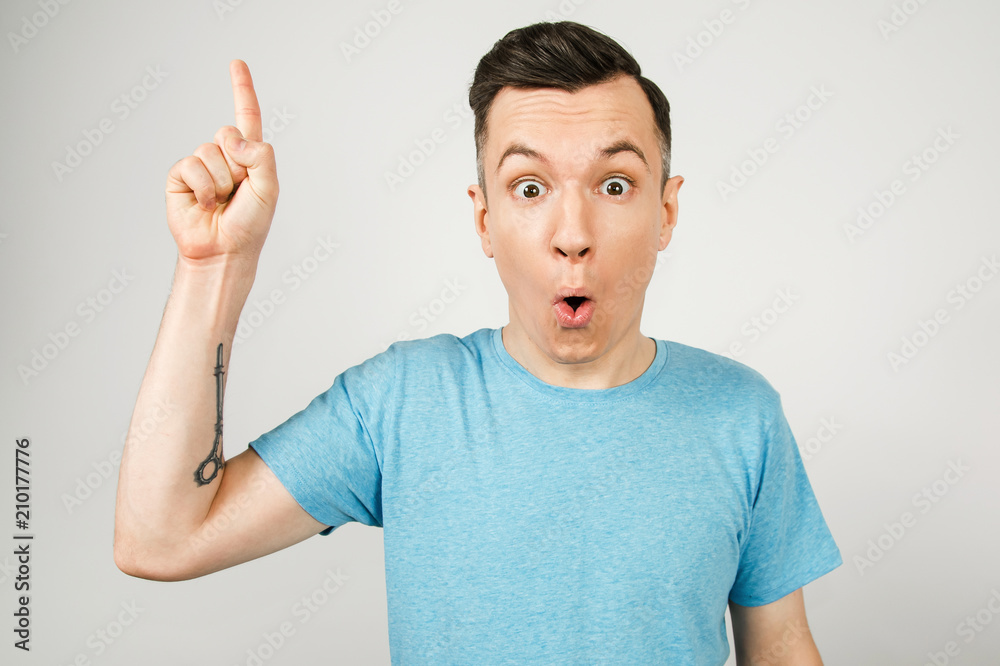 Young surprised guy with finger up, dressed in a blue t-shirt on a light background. Young surprised guy with finger up, dressed in a blue t-shirt on a light background.