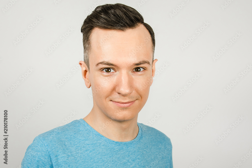 Close up portrait of young smiling guy dressed in a blue t-shirt on a light background. Close up portrait of young smiling guy dressed in a blue t-shirt on a light background.
