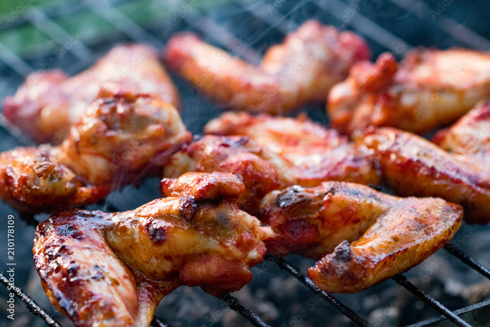 Spicy marinated chicken wings grilling on a summer barbecue with hot flames in a close up view