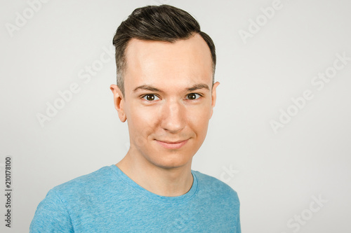 Close up portrait of young smiling guy dressed in a blue t-shirt on a light background. © vika33