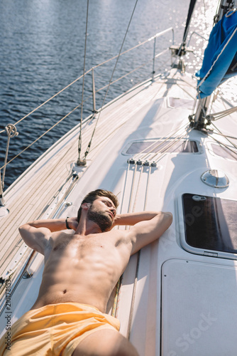 high angle view of shirtless muscular man in swim trunks having sunbath on yacht