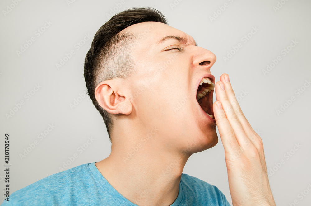 Young yawning guy dressed in a blue t-shirt on a light background. Side  view. Stock Photo | Adobe Stock