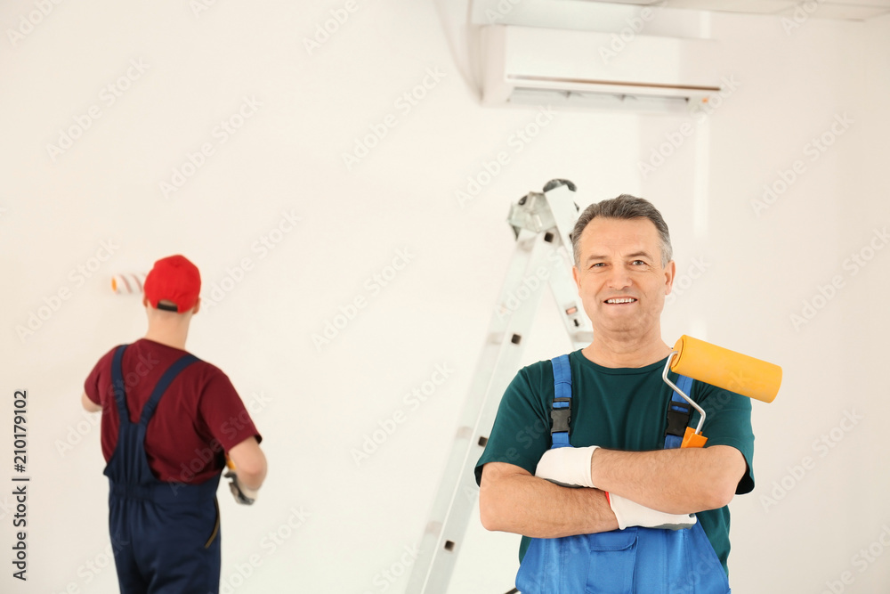 Fototapeta premium Male painter in uniform with roller brush indoors